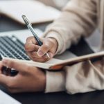Shot of an unrecognisable man writing in a notebook while working from home
